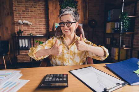 Photo of attractive successful retired woman accountant economist thumb up two hand nice job workstation workspaceの写真素材
