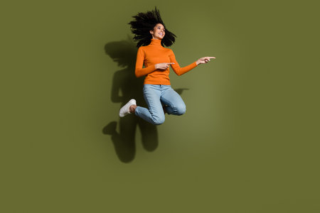 Full length photo of adorable lovely girl wear orange jumper jumping high showing empty space...