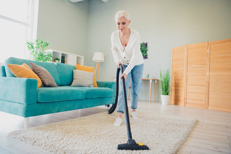 Photo of attractive mature woman dressed casual cardigan use new vacuum cleaner equipment cleaning home house room indoorsの写真素材