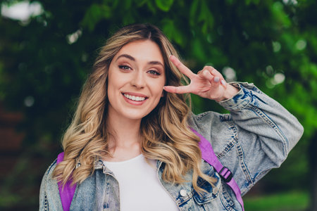 Photo of nice young woman show v-sign eye backpack wear denim jacket walk city center outdoors