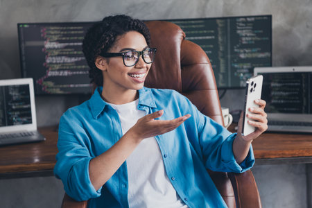 Photo of lovely young lady sit armchair talk video call dressed blue shirt comfortable programmer startup office loft room interiorの写真素材