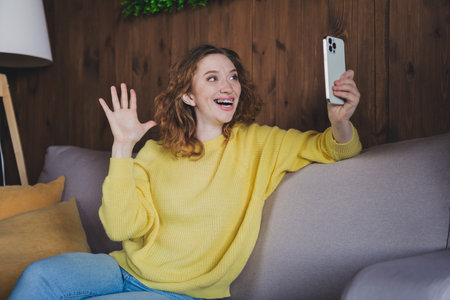 Photo of nice young woman selfie photo wave hand hi wear stylish yellow sweater modern light cozy interior flat indoorsの写真素材