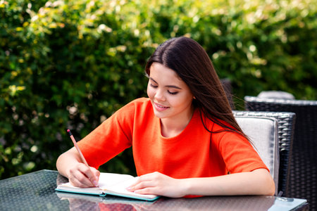 Photo of pretty teen good mood girl sit table cafe write notebook wear red clothes walk outside urban city parkの写真素材