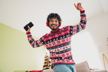 Portrait of nice young man smart phone headphones music wear x-mas sweater holiday atmosphere flat indoorsの写真素材