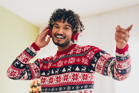 Portrait of nice young man touch headphones good mood wear xmas sweater holiday atmosphere flat indoorsの写真素材
