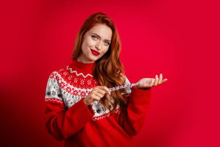 Photo of young satisfied confident lady wearing festive ugly sweater holding christmas tree icicle toy holiday isolated on red color backgroundの写真素材