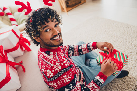High angle view portrait of nice young arab man open giftbox ribbon wear xmas sweater holiday atmosphere flat indoorsの写真素材