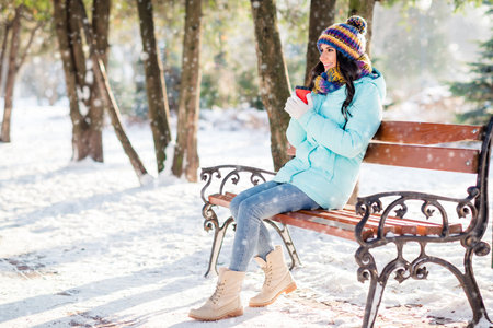 Photo of cute lady hold takeaway cup sit bench drink coffee wear hat scarf gloves coat in winter park outsideの写真素材