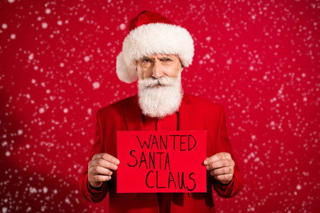 Photo of retired pensioner bearded old man hold hands wanted santa claus card bad mood xmas isolated on red color backgroundの写真素材
