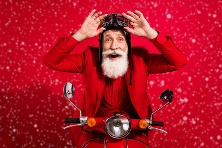 Photo of pretty impressed age gentleman wear new year costume headwear riding motorcycle arms eyewear isolated red color backgroundの写真素材