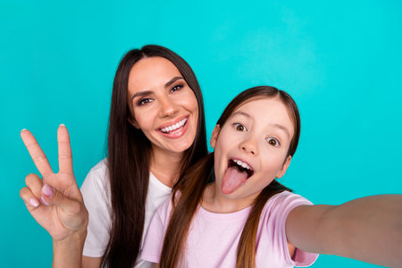 Photo of carefree lovely girl with mommy taking selfie wearing white trendy clothes v-sign isolated on cyan color backgroundの写真素材