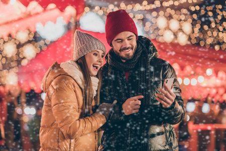Photo of two people students friends browse social media on smartphone point finger x-mas christmas outdoors eventの写真素材