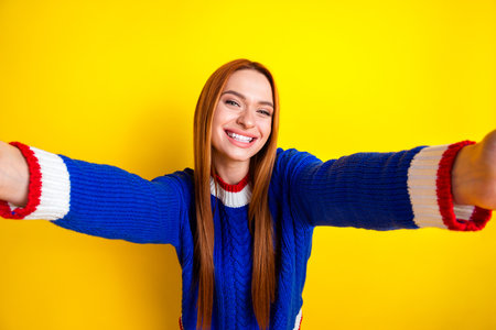Photo portrait of lovely young lady take selfie toothy smile dressed stylish blue knitwear garment isolated on yellow color backgroundの写真素材