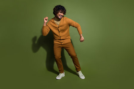Full length photo of handsome young guy dancing have fun dressed stylish brown garment isolated on khaki color backgroundの写真素材