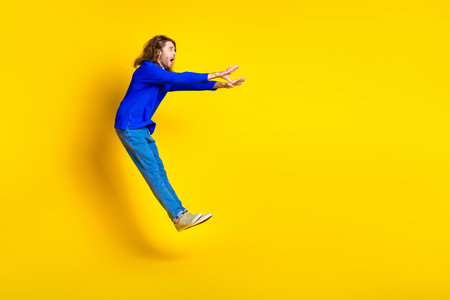 Photo of crazy scared man wear trendy blue clothes fly air empty space isolated on yellow color backgroundの写真素材