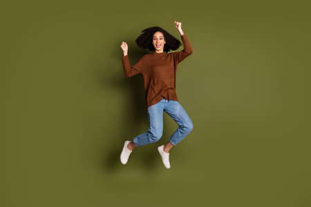 Full size photo of nice young woman jump raise fists wear pullover isolated on khaki color backgroundの写真素材