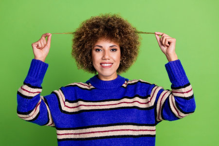 Portrait of good mood gorgeous girl with perming coiffure dressed knit pullover holding curls in hands isolated on green color backgroundの写真素材