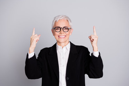 Photo portrait of lovely pensioner lady startup boss point up empty space dressed formalwear specs isolated on gray color backgroundの写真素材