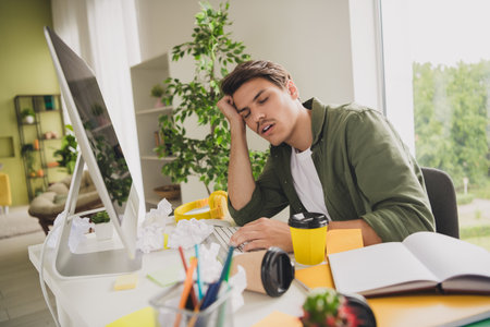 Photo of bored upset hardworking man working modern device drink coffee workplace workstation indoorsの写真素材
