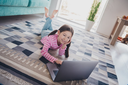 Photo of young funny kid little brunette girl staying at home spending free time laying floor watch...
