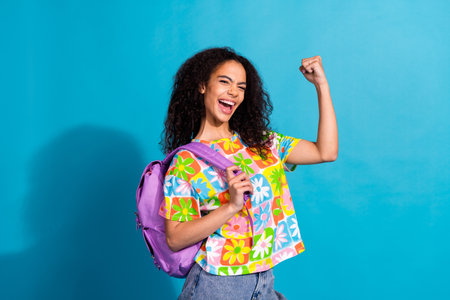 Photo of cheerful lucky lady dressed flower print t-shirt backpack rising fists empty space isolated...