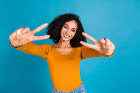 Photo portrait of lovely young lady show v-sign dressed stylish orange garment isolated on blue...