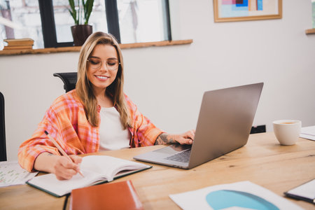 Portrait of pretty young office worker woman laptop write notepad loft interior business center...