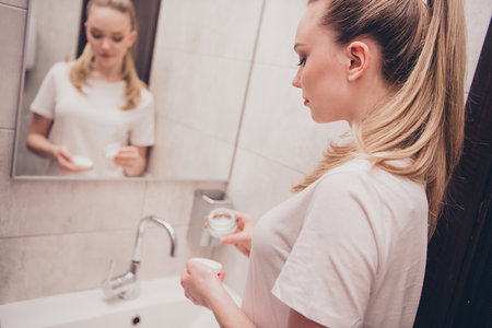 Photo of pretty cheerful lady sleepwear enjoying skin care routine indoors bathroom home houseの写真素材