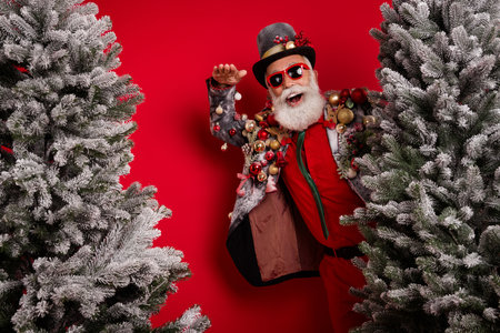 Photo of positive old man wear elegant stylish suit jacket walk xmas forest isolated on red color backgroundの写真素材