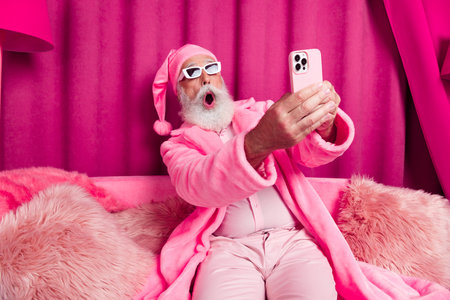 Photo of impressed funny santa claus sit fluffy sofa use fast speed wifi on gadget e shop in pink color room interior wear hat robeの写真素材