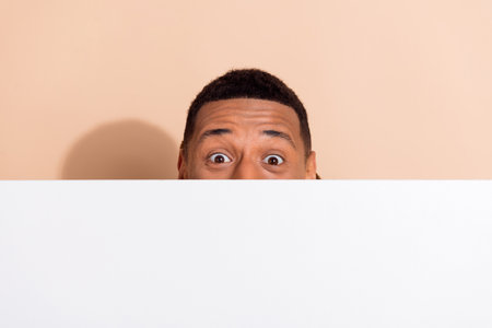 Photo of crazy funny man wear trendy clothes hiding white wall empty space isolated on beige color backgroundの写真素材