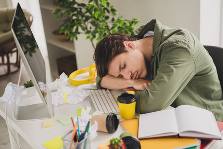 Photo of bored sleepy man lying table hard work workstation workspace indoorsの写真素材