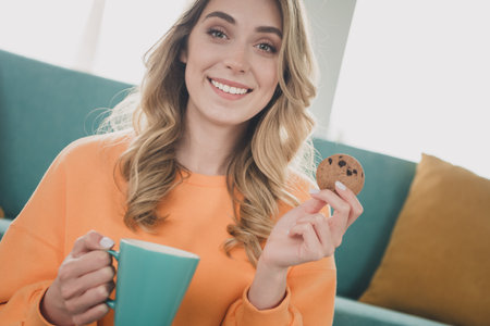 Photo portrait of nice cheerful girl sit floor eat cookie drink tea dressed orange garment spend pastime spacious house indoors roomの写真素材