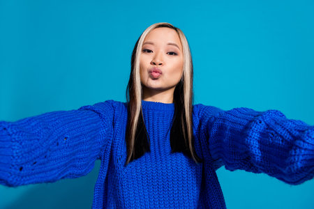 Photo portrait of attractive young woman selfie photo kissing dressed stylish knitwear clothes isolated on blue color backgroundの写真素材