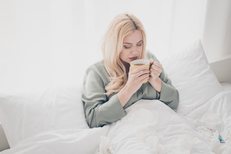 Photo of pretty young woman drink tea bed silky pajama white interior bedroom apartment indoorsの写真素材