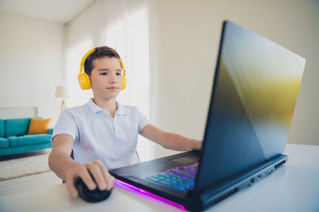 Photo of cute schoolboy play games gaming laptop wear t-shirt modern interior apartment indoorsの写真素材