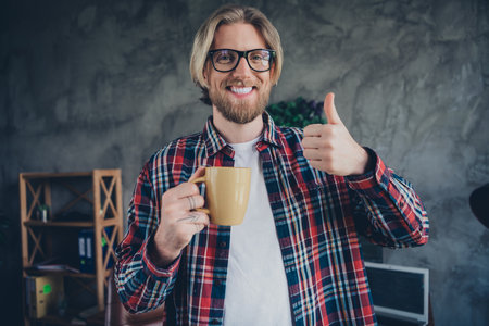 Portrait of young blond hair man friendly office manager holding cup tea indoors modern office showing high rate feedback about first day new jobの写真素材