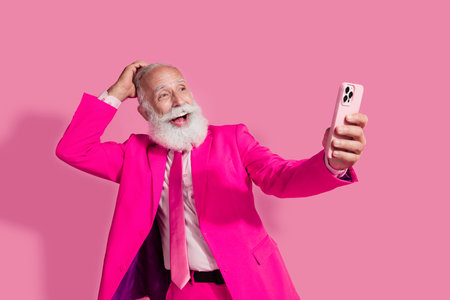 Photo of serious old cool man gentleman boyfriend surprised hold gadget wear stylish pink suit isolated over pastel color backgroundの写真素材