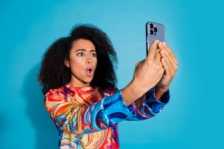 Photo portrait of pretty young girl hold gadget shocked wear trendy colorful outfit isolated on blue...