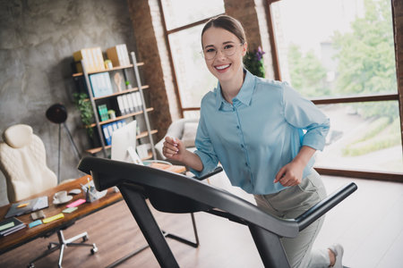 Photo of happy positive lady recruiter dressed shirt running treadmill indoors workplace workstation...