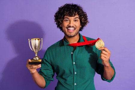 Photo of handsome arabian guy with wavy haircut wearing green showing his first place medal casual shirt isolated on violet color backgroundの写真素材