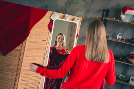 Photo of attractive young woman choose dress dressed red christmas outfit cozy day light home party decoration interior living roomの写真素材