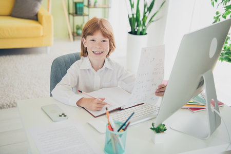 Portrait of cute charming smart clever learner boy sitting chair table doing hometask flat indoorsの写真素材