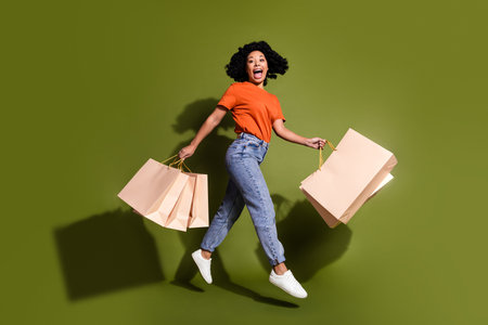 Full size photo of pretty young woman jump run bags wear t-shirt isolated on khaki color backgroundの写真素材