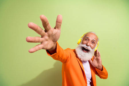 Portrait of aged man performer touch headphones raise arm you wear orange suit isolated on green...