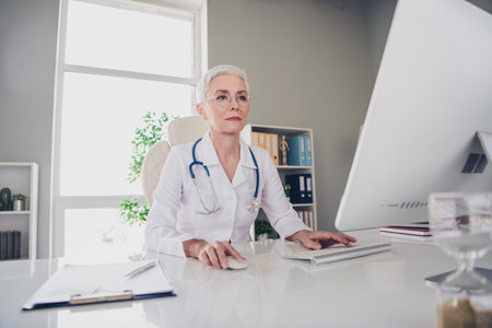 Photo of family doc successful professional mature lady doctor work computer wear white lab coat modern office clinic indoorsの写真素材