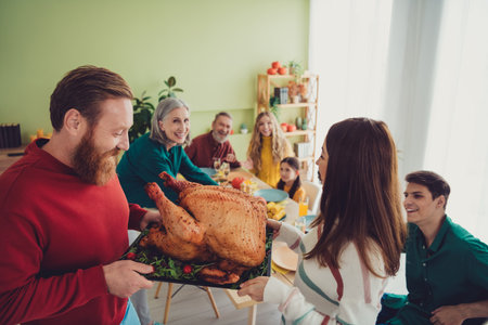 Photo of cheerful smiling people serving table holiday stuffed baked tasty traditional turkey thanksgiving day indoorsの写真素材