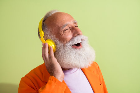 Portrait of funky eccentric grandfather closed eyes touch headphones wear orange suit isolated on green color backgroundの写真素材
