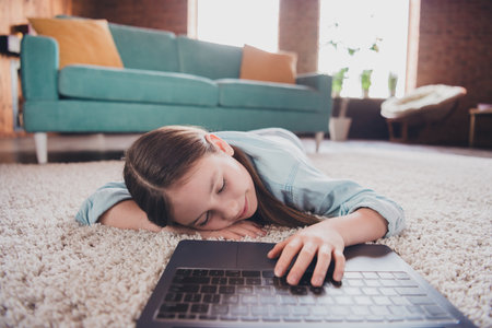 Portrait of cute little girl lying floor sleep video call lesson laptop loft interior modern flat...