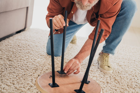 Cropped photo of senior male repair chair household dressed brown outfit cozy day light home interior living roomの写真素材